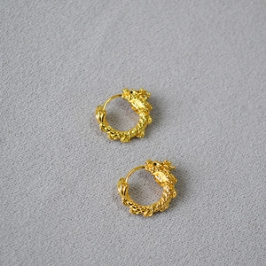 Détail macro de boucles d'oreilles dragon en laiton doré avec écailles et textures gravées