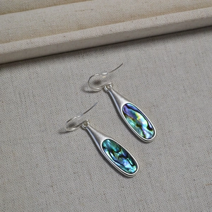 Macro detail of silver drop earrings with colorful abalone shell inlays on fabric