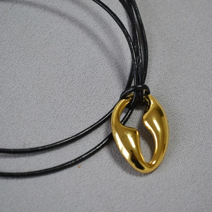 Macro shot of an irregular organic gold pendant with a polished finish on black cord