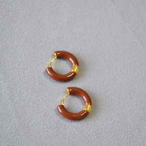 Détail de boucles d'oreilles en émail rouge et laiton doré sur une surface grise