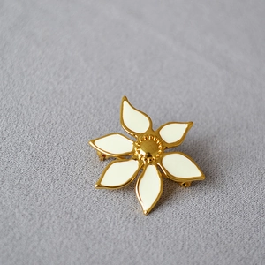 Detail of white enamel flower brooch with gold plated edges on grey fabric