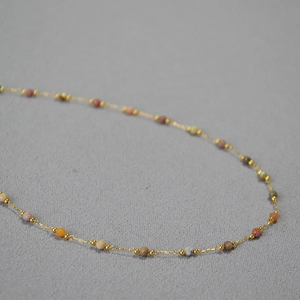 Détail d'un collier fin doré avec perles en pierre naturelle facettées multicolores
