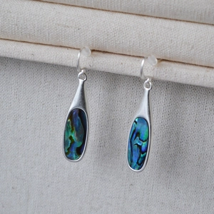 Close-up of teardrop shell earrings with iridescent abalone inlay on a fabric background