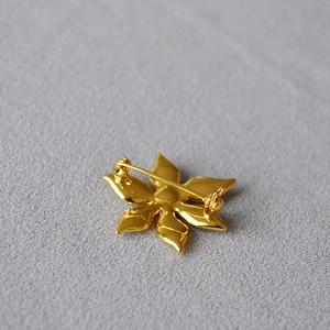 Elegant gold flower brooch back view with safety pin clasp on grey fabric background