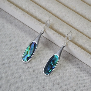 Macro shot of silver drop earrings with rainbow abalone shell inlay on a jewelry tray