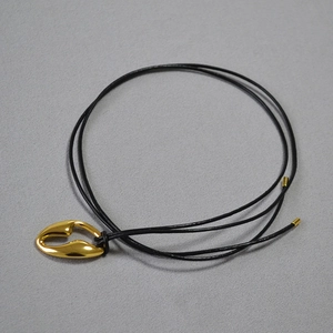 Detail of minimalist gold hollow teardrop pendant with black leather cord on fabric