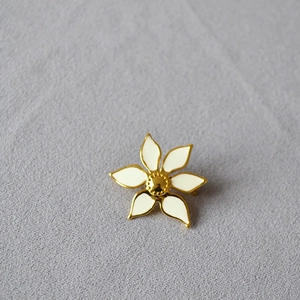 Detailed close-up of a white enamel six-petal flower brooch with elegant gold metal edges