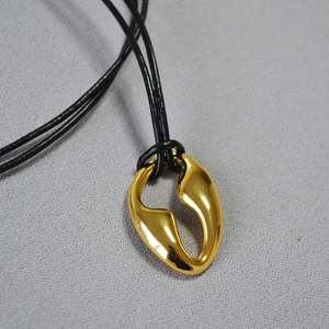 Detailed macro view of abstract golden asymmetric pendant on black braided cord necklace