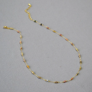 Détail d'un collier doré fin avec des perles en pierre naturelle facettées multicolores