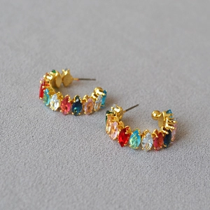 Détail de boucles d'oreilles créoles dorées avec zircons multicolores sur tissu gris