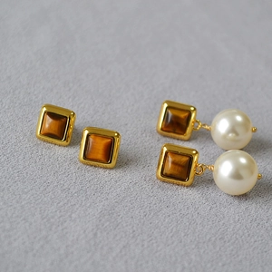 Détail de boucles d'oreilles géométriques en oeil de tigre et perles sur tissu gris