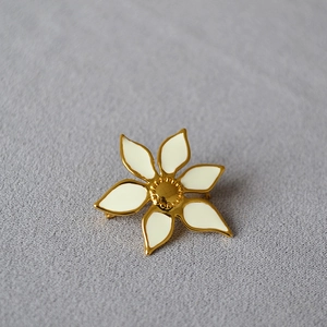 Elegant white enamel flower brooch with gold plating on a textured grey fabric background