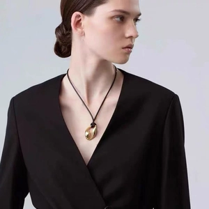 Artistic gold organic fluid pendant necklace with slim black cord on elegant model