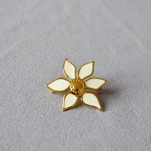 Elegant gold-plated brass brooch featuring a white enamel flower on textured fabric
