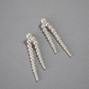 Détails des boucles d'oreilles à pompons de perles blanches et métal doré sur tissu