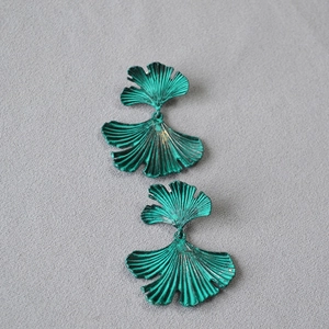 Retro oxidized green ginkgo leaf stud earrings with textured metallic finish on fabric