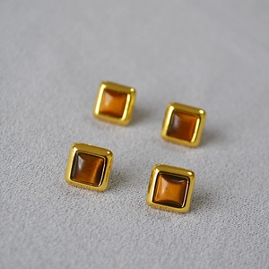 Détail macro de boucles d'oreilles carrées en oeil de tigre avec monture dorée polie
