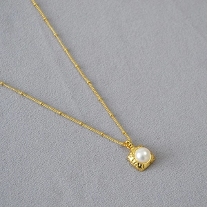 Gros plan d'un collier avec pendentif carré doré orné d'une perle d'eau douce blanche