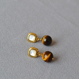 Detailed view of geometric earrings featuring square mother of pearl and tiger eye beads