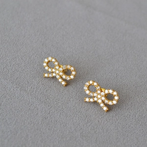 Elegant gold bow earrings for women with shimmering pavé crystal stones on grey fabric
