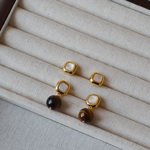Detail of square mother-of-pearl studs and tiger eye drop earrings in gold finish