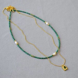 Detailed view of layered gold necklace with malachite beads and emerald square pendant