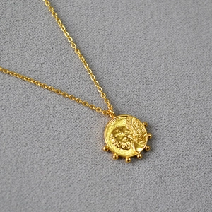 Gros plan du pendentif pièce ange doré avec relief embossé sur une chaîne vintage