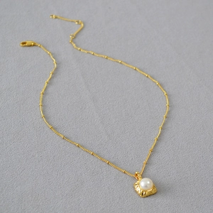Gros plan d'un collier en laiton doré avec pendentif carré martelé et perle d'eau douce