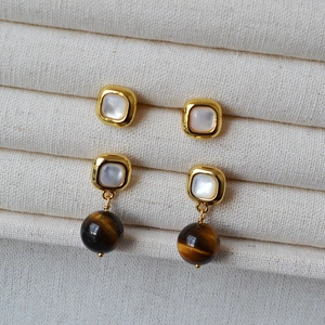 Detail of square shell studs and tiger eye stone drop earrings on canvas texture