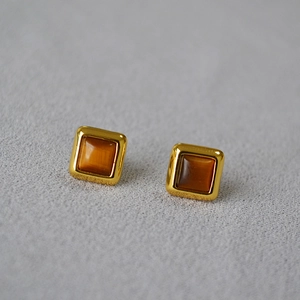 Vue rapprochée de boucles d'oreilles carrées dorées avec pierre œil de tigre et tige en argent 925