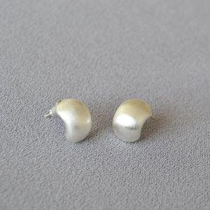 Macro detail of silver bean earrings featuring a minimalist brushed matte metal finish