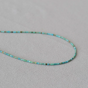 Macro shot of ultra-fine beaded necklace with turquoise and lapis lazuli on gray fabric