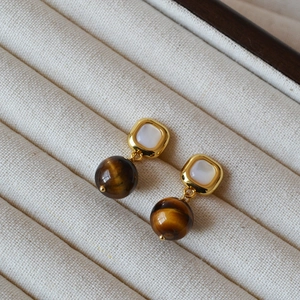 Macro detail of geometric earrings featuring white mother-of-pearl and tiger eye stone beads