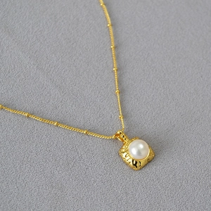 Détail macro du pendentif carré doré avec texture martelée et perle d'eau douce blanche