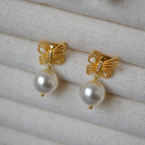 Close-up of gold bow earrings with micro-inlaid crystals and elegant pearl drops