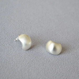 Macro detail of silver bean earrings with fine brushed texture on soft grey fabric
