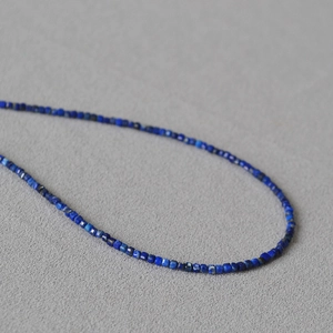Minimalistische facettierte Lapislazuli Perlenkette auf grauem strukturiertem Stoff