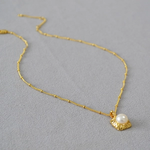 Détail du collier en laiton doré avec un pendentif carré orné d'une perle d'eau douce
