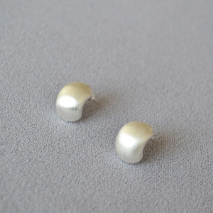Macro shot of silver brushed metal stud earrings with a minimalist arc design