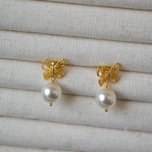 Macro detail of gold butterfly earrings with bow pattern, sparkling zircon, and white pearl
