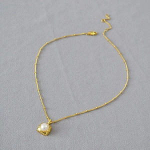 Détail d'un pendentif carré en laiton doré avec perle d'eau douce sur chaîne fine