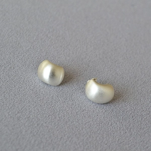 Macro detail of silver bean earrings with matte brushed finish on purple textured fabric