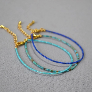 Detailed shot of bohemian style lapis and turquoise thin beaded bracelets with gold clasps