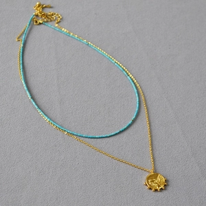 Détail du collier à deux rangs avec perles turquoise et pendentif pièce d'or