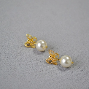 Detail of gold bow earrings featuring zircon accents and a dangling white pearl drop