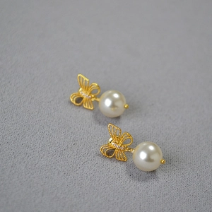Detailed view of bow stud earrings with gold filigree and large white round pearls