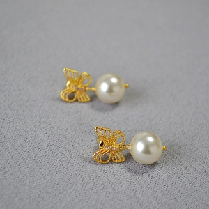 Macro detail of bow-shaped gold stud earrings with white pearl and pink zircon