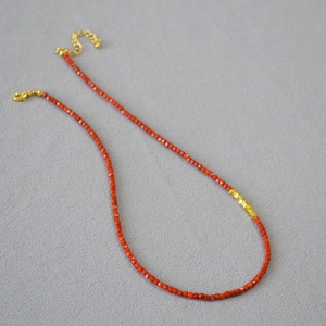Macro view of red agate square beads and golden spacers on a dainty beaded necklace