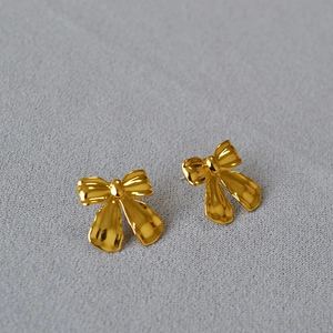 Polished gold-plated bow-shaped stud earrings on grey textured fabric background