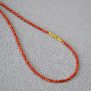 Macro detail of faceted red agate beads and golden accents on a delicate beaded necklace
